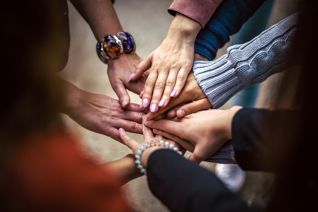Das Bild zeigt mehrere Hände, die übereinandergelegt sind – ein starkes Symbol für Gemeinschaft, Zusammenhalt und Teamarbeit. Die Hände gehören zu unterschiedlichen Personen, was Vielfalt und Kooperation ausdrückt. Solche Gesten werden oft bei gemeinsamen Aktionen, Nachbarschaftsinitiativen oder Team-Events verwendet, um Verbundenheit zu zeigen.